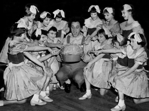 Black and white photograph of entertainer Ken Dodd smiling with a group of young dancers.